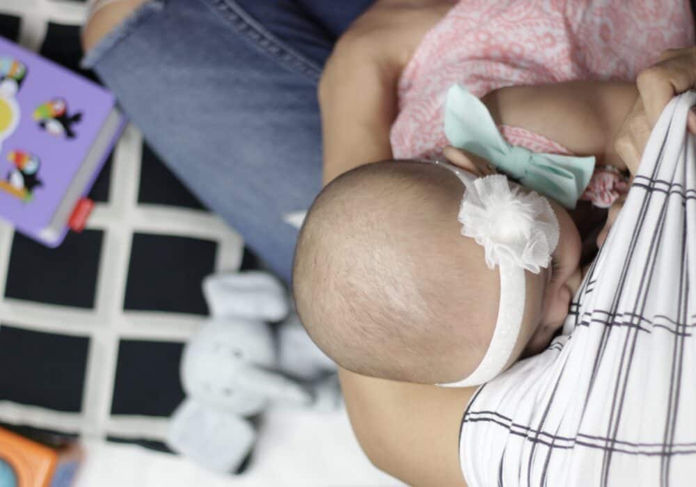 A baby is being breastfed by a Mom Boss™ 4-IN-1 Multi-Use Nursing Cover & Scarf.