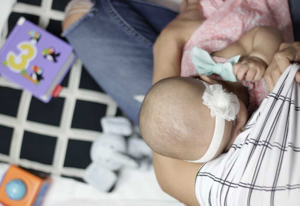 A baby is being breastfed by a woman wearing the Mom Boss™ 4-IN-1 Multi-Use Nursing Cover & Scarf.