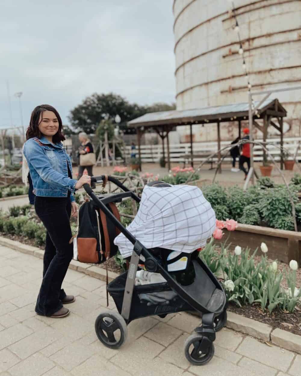 A woman pushing a Mom Boss™ 4-IN-1 Multi-Use Nursing Cover & Scarf in front of a silo.