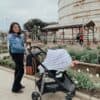 A woman pushing a Mom Boss™ 4-IN-1 Multi-Use Nursing Cover & Scarf in front of a silo.