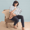 A woman is sitting on a chair holding the Mom Boss™ 4-IN-1 Multi-Use Nursing Cover & Scarf.