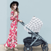 A woman in a floral dress pushing a Mom Boss™ 4-IN-1 Multi-Use Nursing Cover & Scarf stroller.