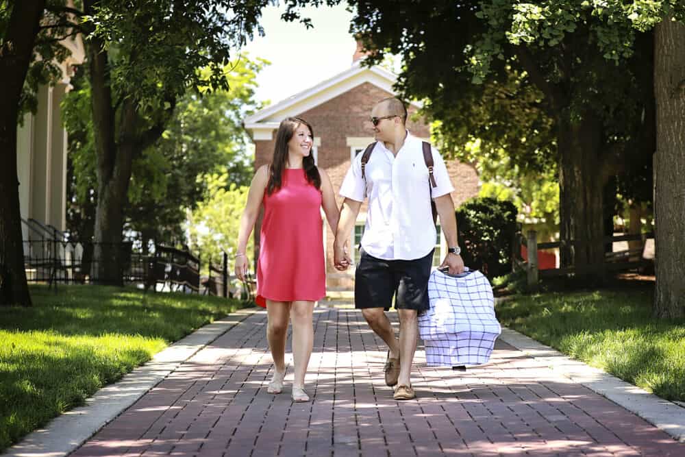 A man and woman walking down a brick walkway, carrying the Mom Boss™ 4-IN-1 Multi-Use Nursing Cover & Scarf.