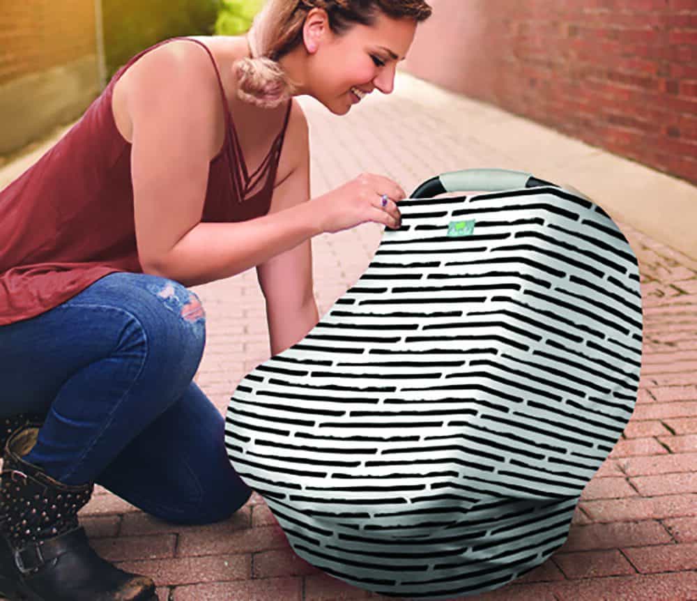 A woman kneeling down next to a Mom Boss™ 4-IN-1 Multi-Use Nursing Cover & Scarf.