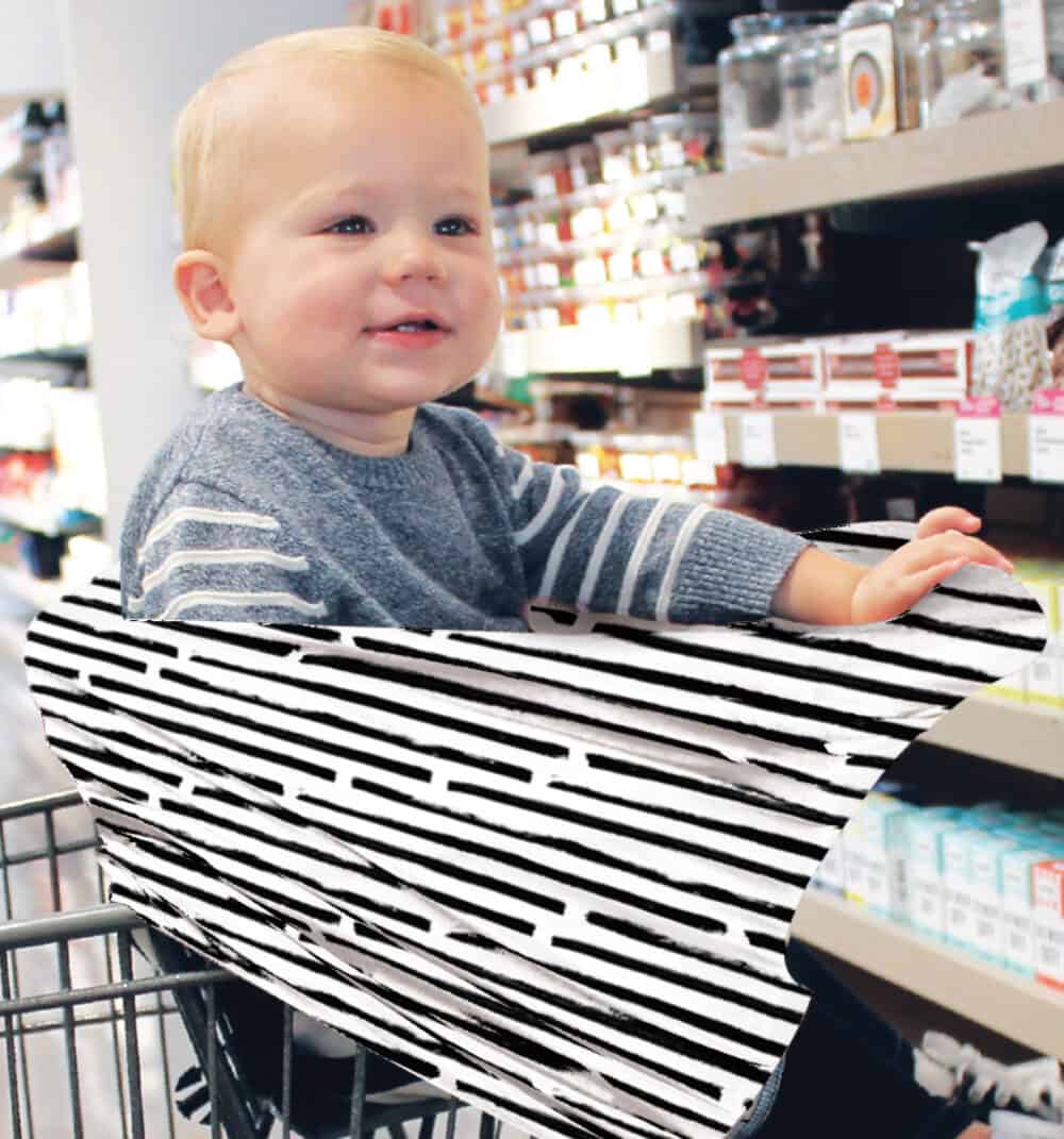 A baby sitting in a Mom Boss™ 4-IN-1 Multi-Use Nursing Cover & Scarf with a black and white stripe.