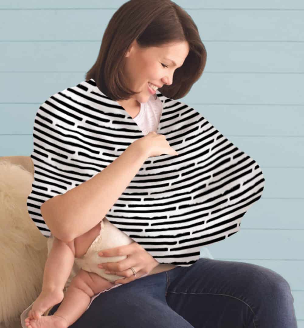 A woman holding a baby in a Mom Boss™ 4-IN-1 Multi-Use Nursing Cover & Scarf.