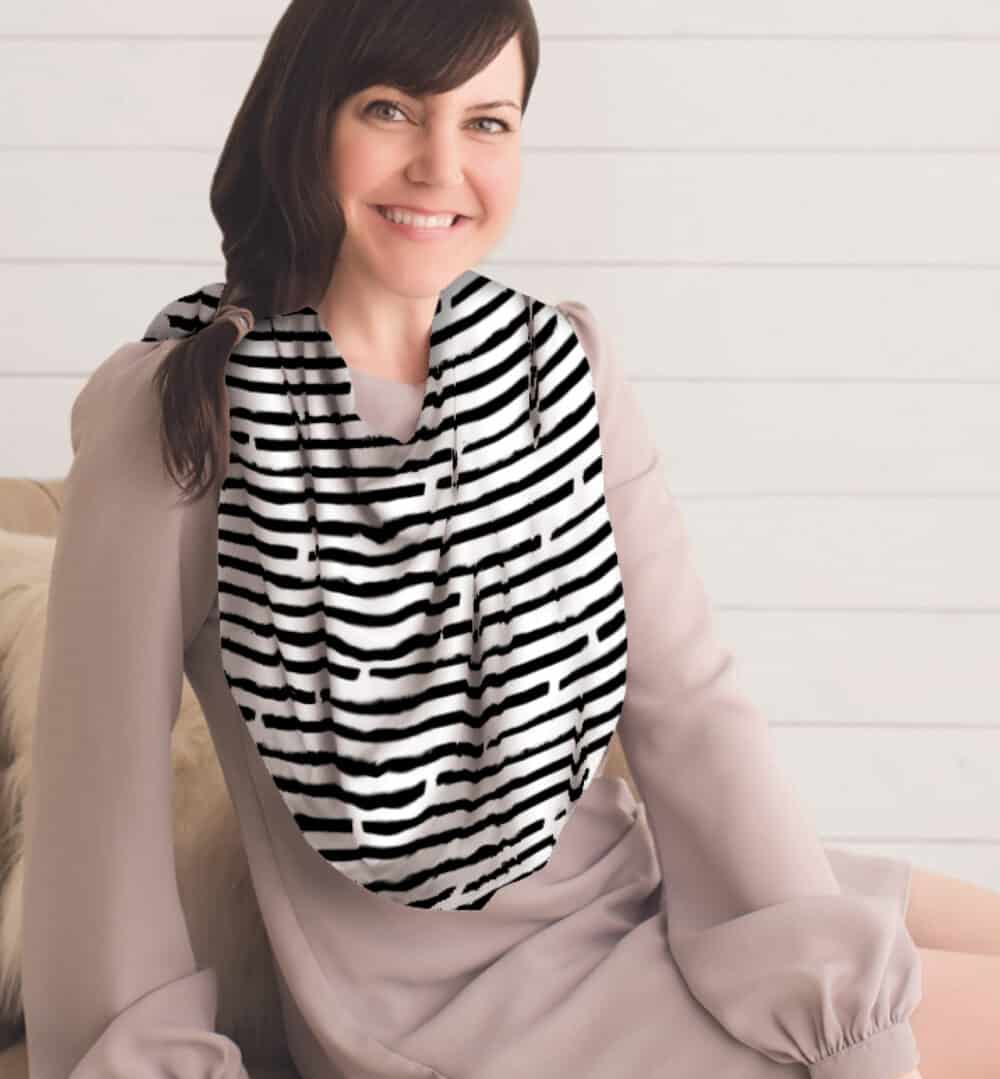 A woman sitting on a couch wearing a Mom Boss™ 4-IN-1 Multi-Use Nursing Cover & Scarf.