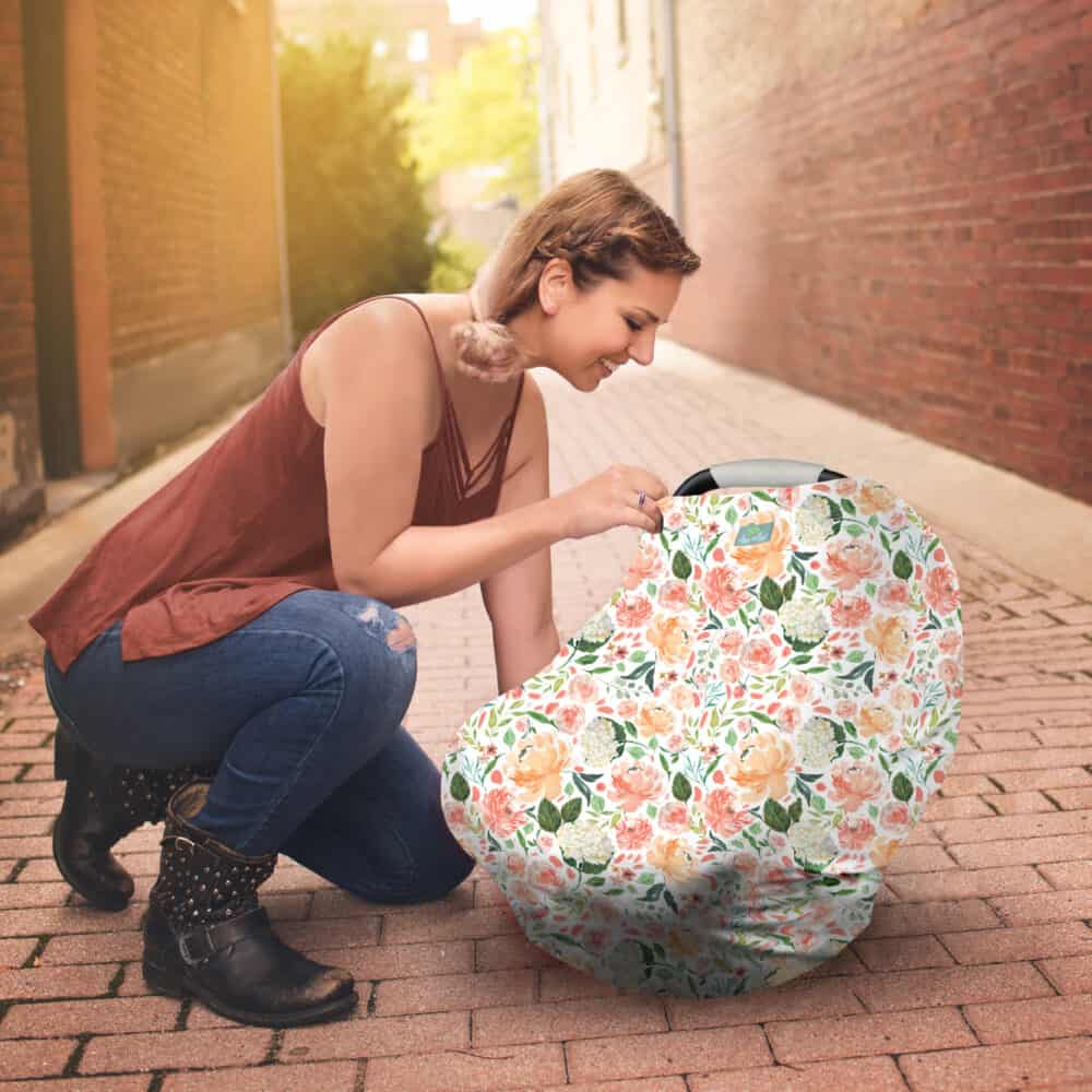 A woman kneeling on the sidewalk with a Mom Boss™ 4-IN-1 Multi-Use Nursing Cover & Scarf.
