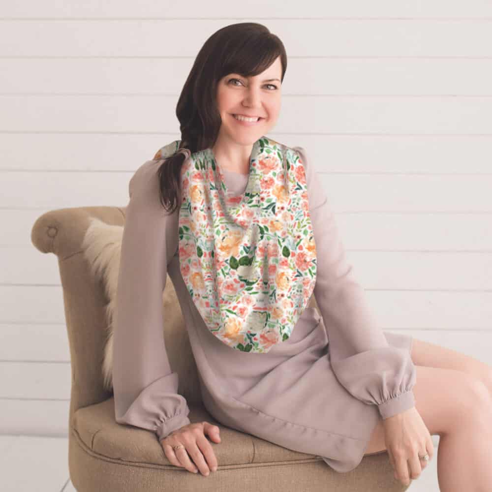 A woman sitting on a chair wearing the Mom Boss™ 4-IN-1 Multi-Use Nursing Cover & Scarf.