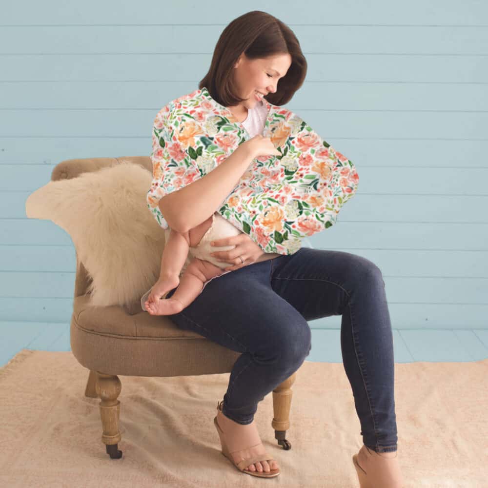 A woman sitting on a chair with a Mom Boss™ 4-IN-1 Multi-Use Nursing Cover & Scarf in her arms.