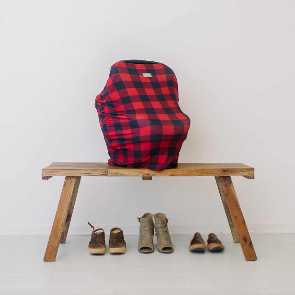 A red and black plaid Mom Boss™ 4-IN-1 Multi-Use Nursing Cover & Scarf on a wooden bench.