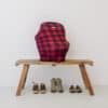 A red and black plaid Mom Boss™ 4-IN-1 Multi-Use Nursing Cover & Scarf on a wooden bench.