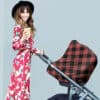 A woman in a plaid dress is standing next to a Mom Boss™ 4-IN-1 Multi-Use Nursing Cover & Scarf stroller.