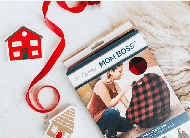 The Mom Boss™ 4-IN-1 Multi-Use Nursing Cover & Scarf is on a rug with a red plaid blanket.