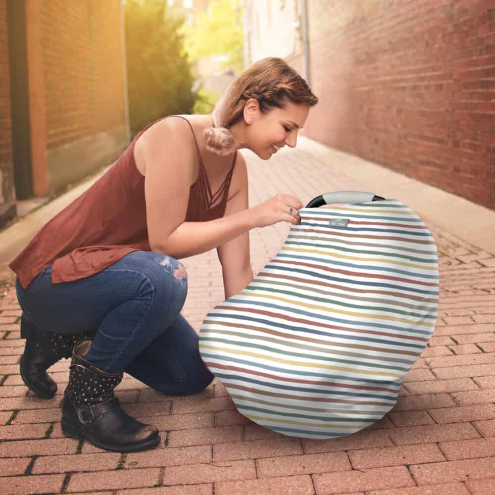 A woman kneeling down next to a Mom Boss™ 4-IN-1 Multi-Use Nursing Cover & Scarf.