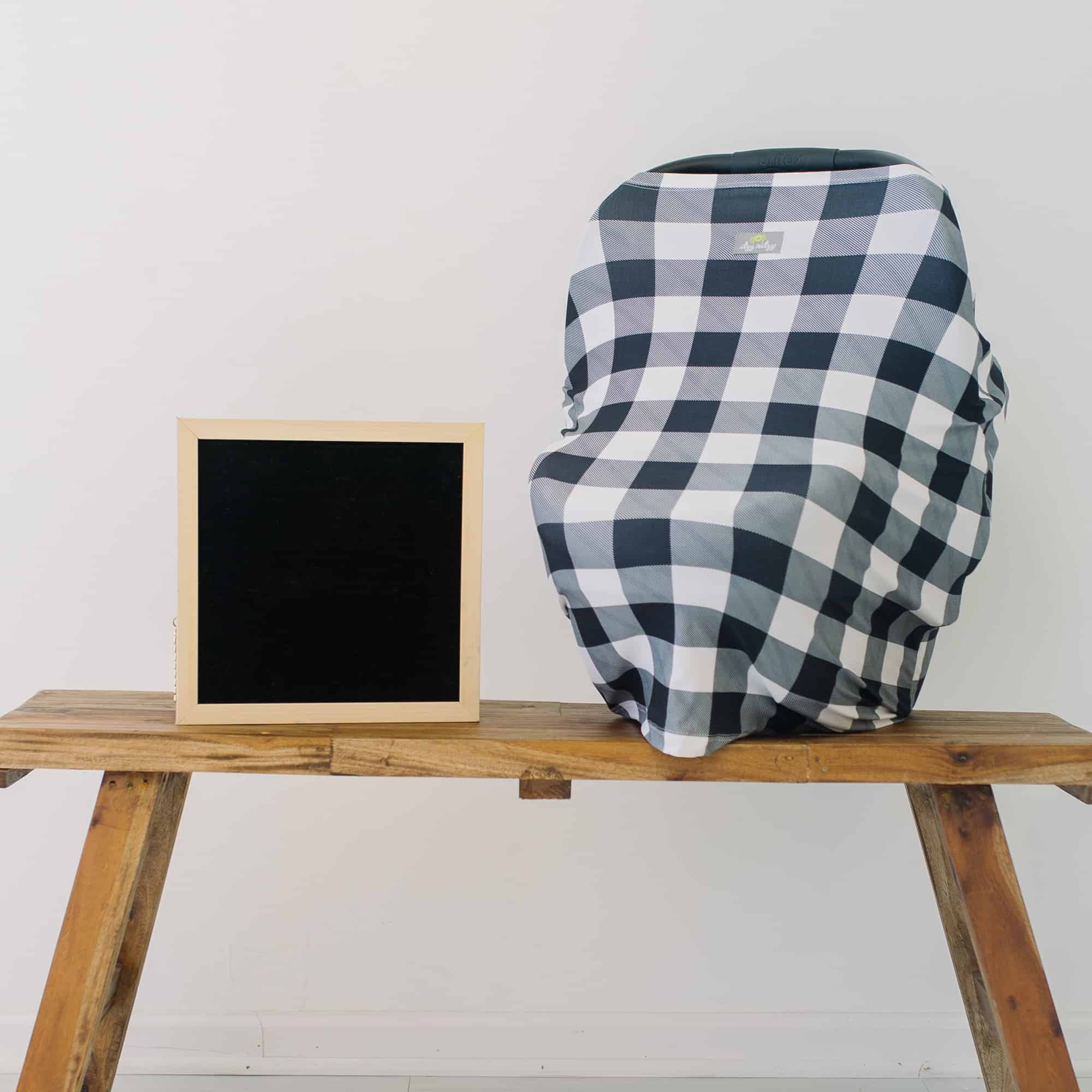 A black and white plaid Mom Boss™ 4-IN-1 Multi-Use Nursing Cover & Scarf on a wooden bench.