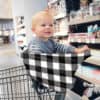 A baby sitting in a shopping cart with a Mom Boss™ 4-IN-1 Multi-Use Nursing Cover & Scarf.