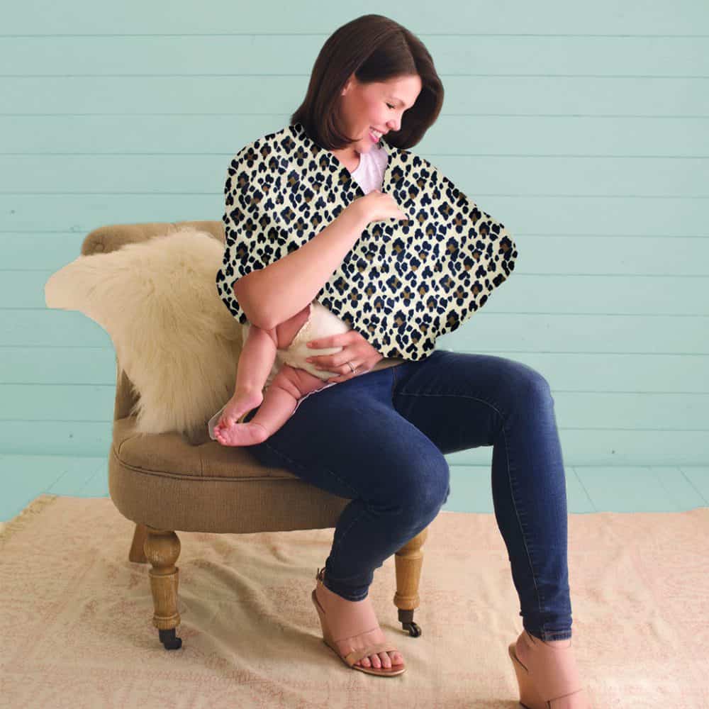 A woman sitting on a chair with a Mom Boss™ 4-IN-1 Multi-Use Nursing Cover & Scarf wrap.
