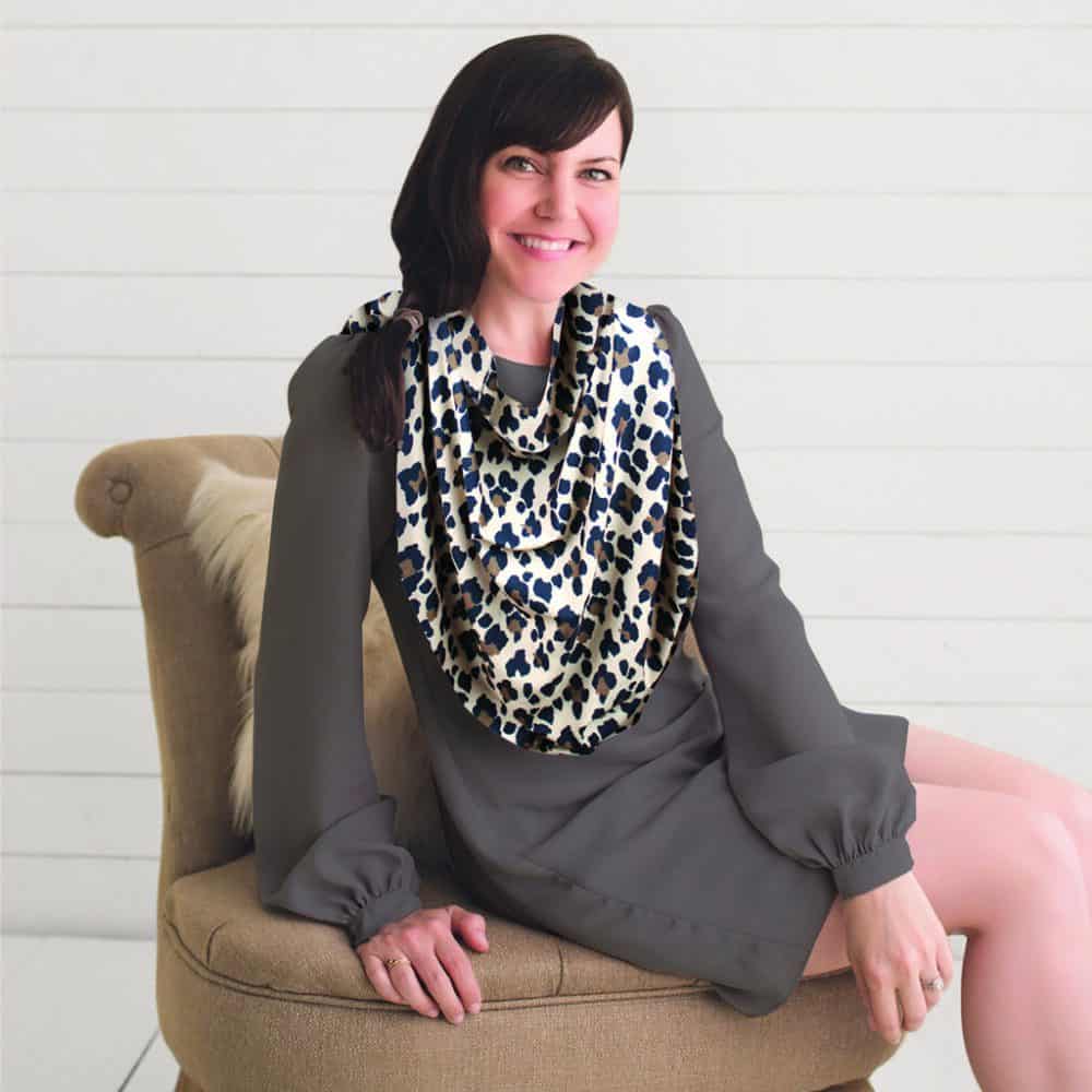 A woman sitting on a chair wearing a Mom Boss™ 4-IN-1 Multi-Use Nursing Cover & Scarf.