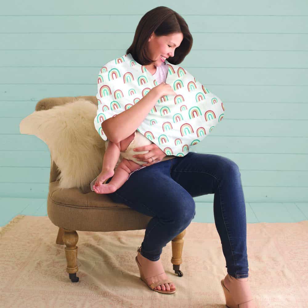 A woman is sitting on a chair holding a Mom Boss™ 4-IN-1 Multi-Use Nursing Cover & Scarf.