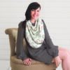 A woman sitting on a chair wearing the Mom Boss™ 4-IN-1 Multi-Use Nursing Cover & Scarf.