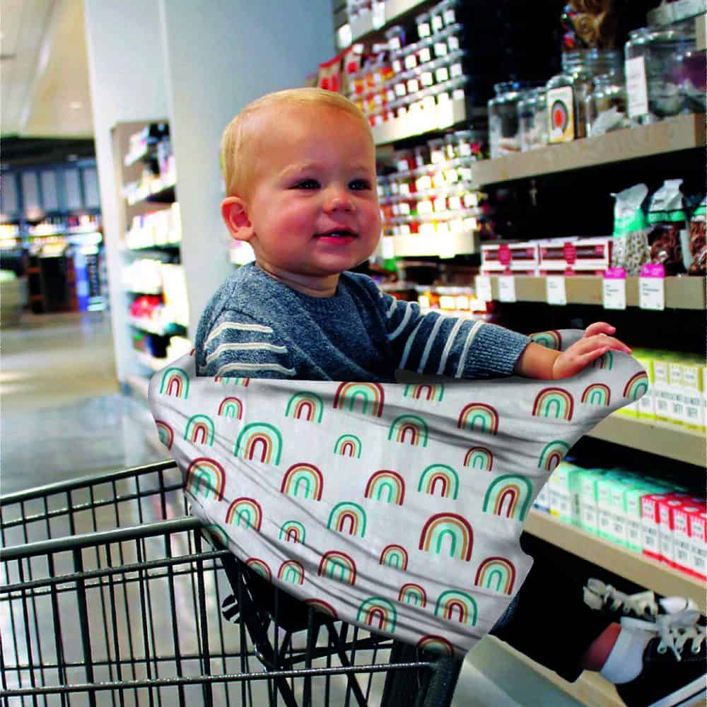 A baby sitting in a Mom Boss™ 4-IN-1 Multi-Use Nursing Cover & Scarf in a grocery store.