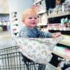 A baby sitting in a Mom Boss™ 4-IN-1 Multi-Use Nursing Cover & Scarf in a grocery store.