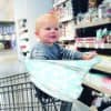 A baby sitting in a shopping cart in a grocery store while using the Mom Boss™ 4-IN-1 Multi-Use Nursing Cover & Scarf.