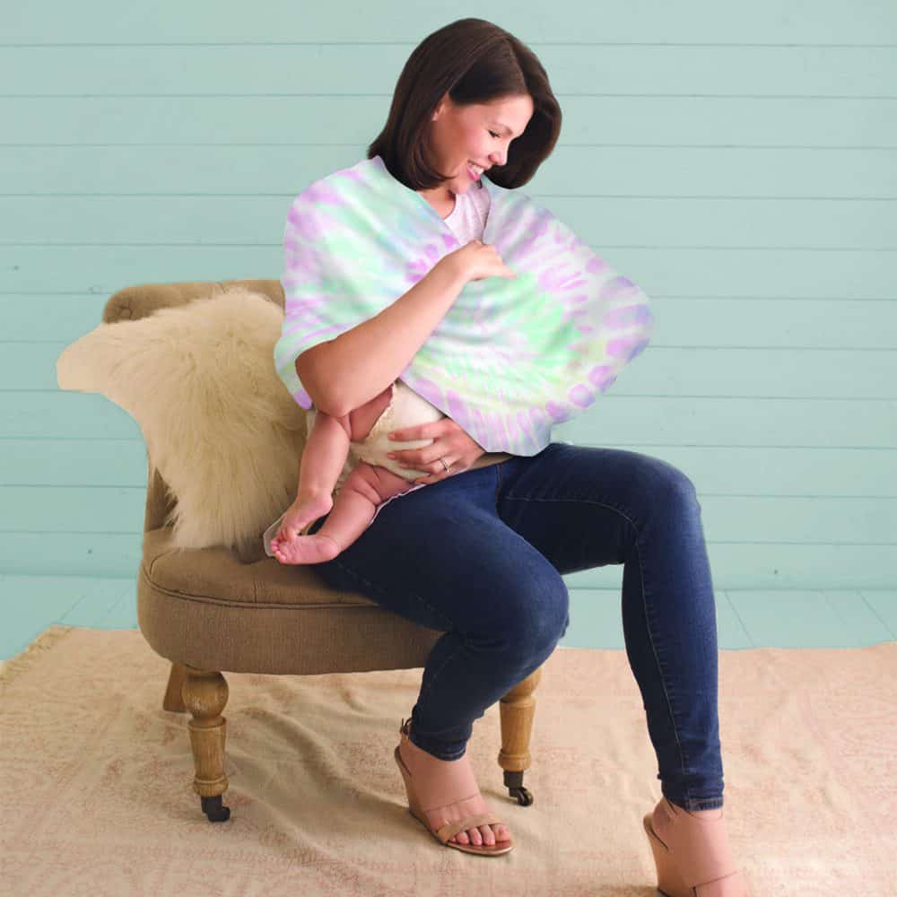 A woman sitting on a chair holding a baby in a Mom Boss™ 4-IN-1 Multi-Use Nursing Cover & Scarf wrap.