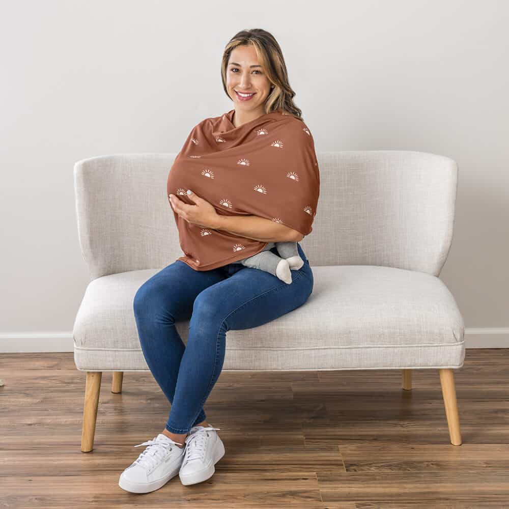 A woman sitting on a couch wearing a Mom Boss™ 4-IN-1 Multi-Use Nursing Cover & Scarf.