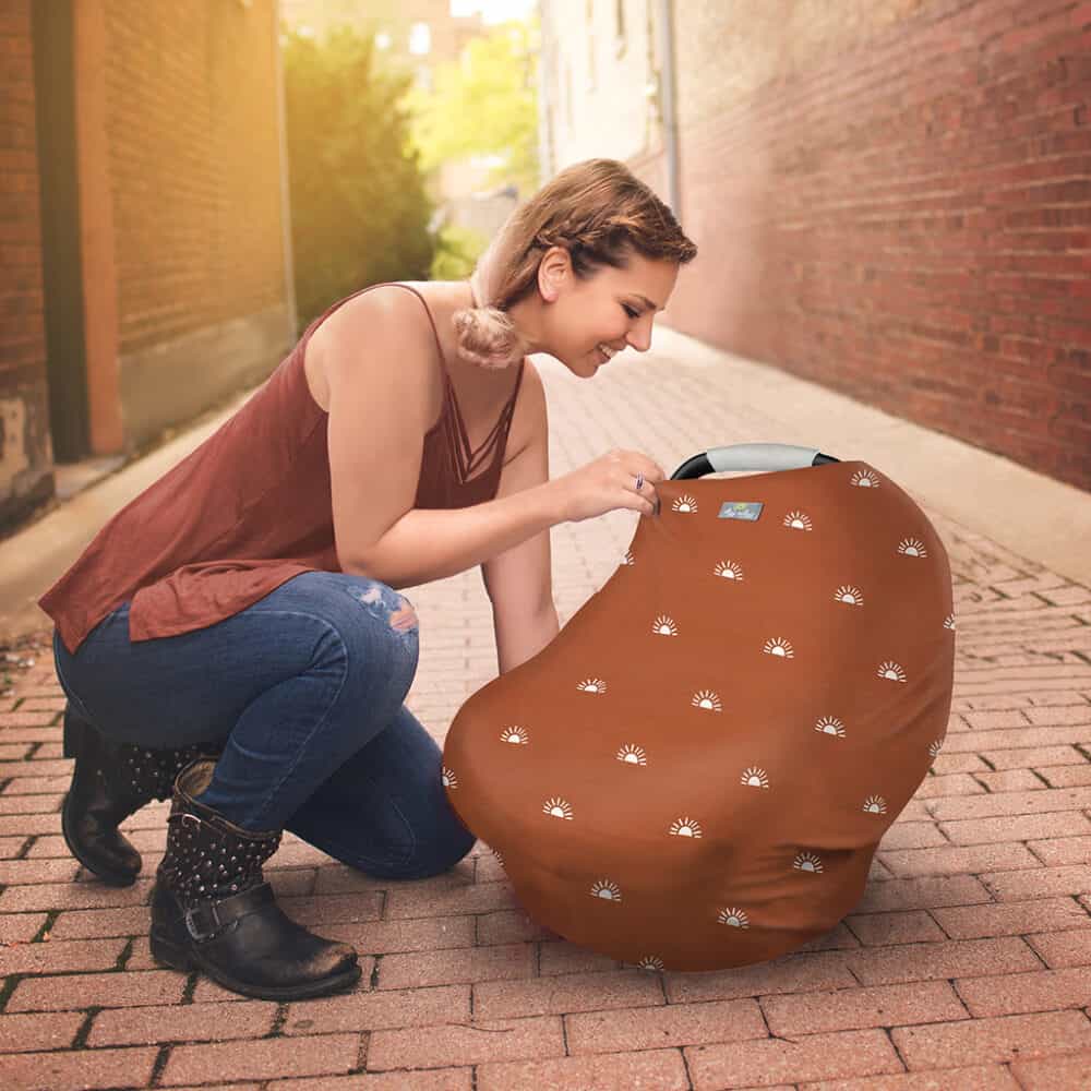A woman kneeling on the sidewalk with a Mom Boss™ 4-IN-1 Multi-Use Nursing Cover & Scarf.