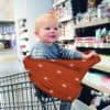 A baby sitting in a Mom Boss™ 4-IN-1 Multi-Use Nursing Cover & Scarf in a grocery store.