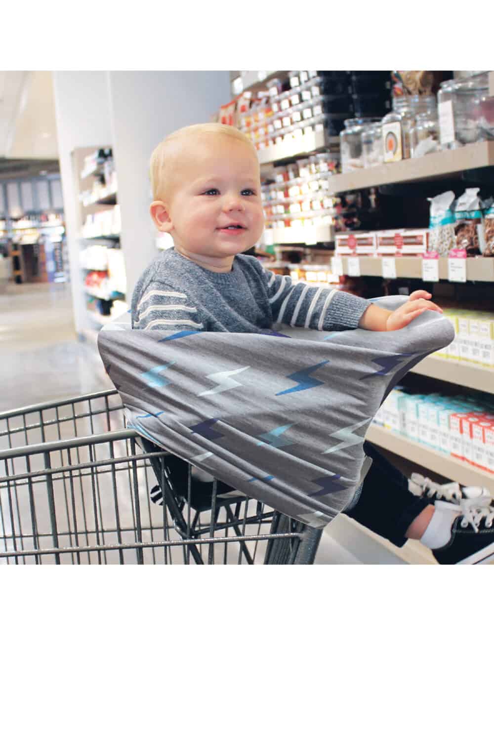 A baby sitting in a Mom Boss™ 4-IN-1 Multi-Use Nursing Cover & Scarf in a grocery store.