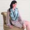 A woman sitting on a chair wearing the Mom Boss™ 4-IN-1 Multi-Use Nursing Cover & Scarf.
