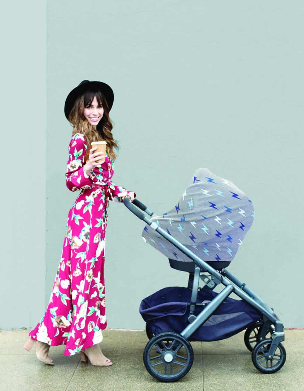 A woman pushing a stroller with the Mom Boss™ 4-IN-1 Multi-Use Nursing Cover & Scarf and a cup of coffee.