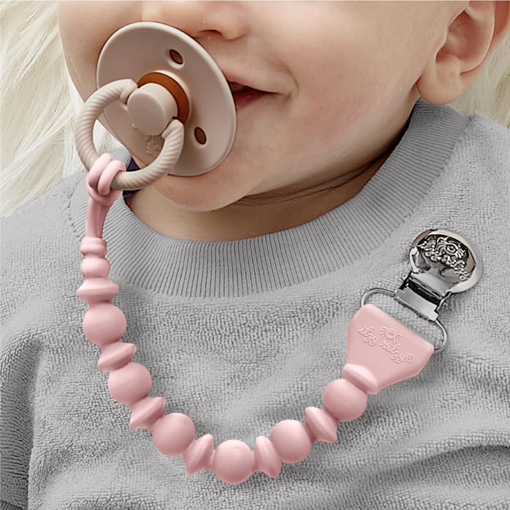 A baby with a pink pacifier clip attached to their gray outfit holds a pacifier in their mouth.