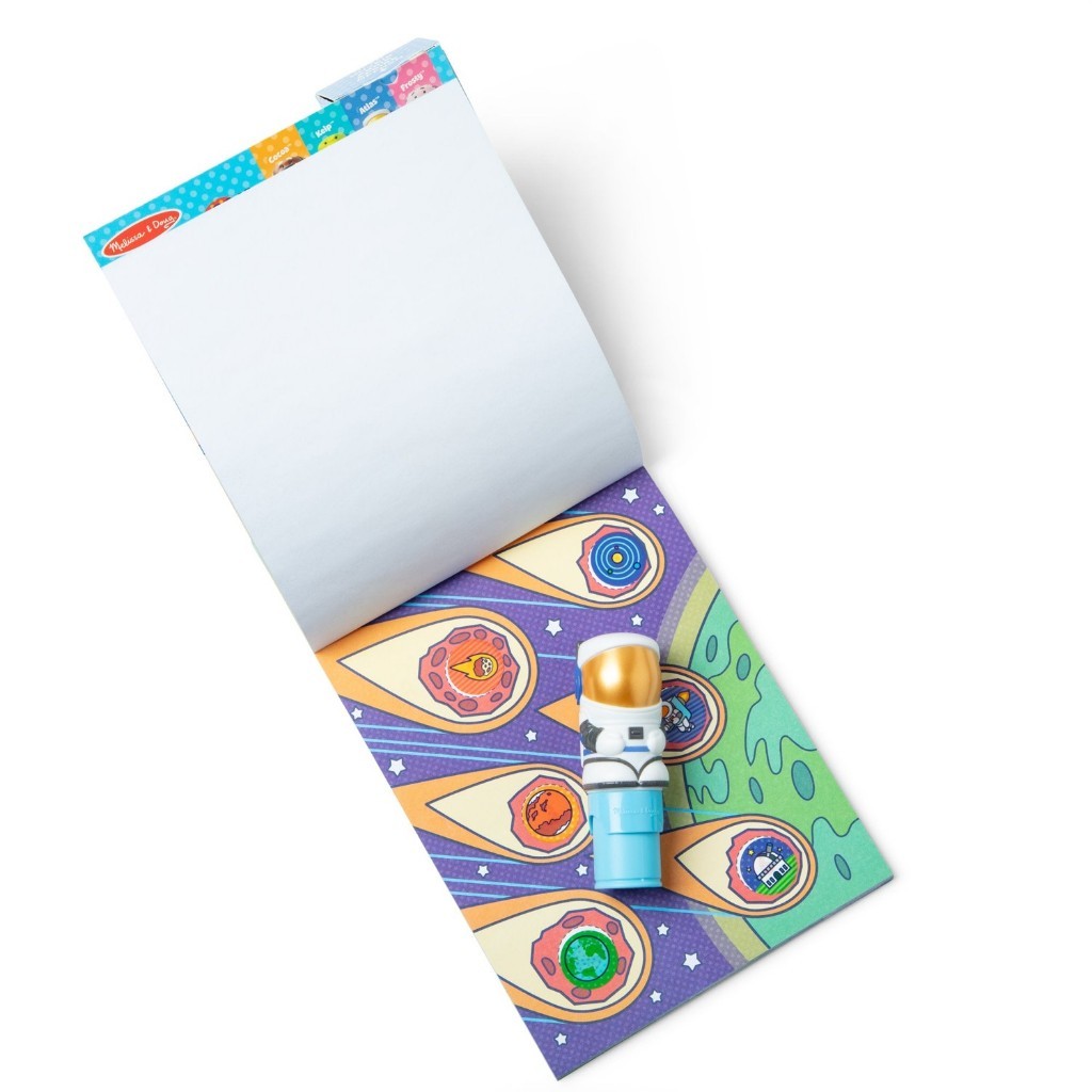 melissadoug-stickerwow-2 A Melissa & Doug Sticker WOW Activity Pad is open, showing its blank white pages, a vibrant space-themed sheet, and a small astronaut marker resting on top.