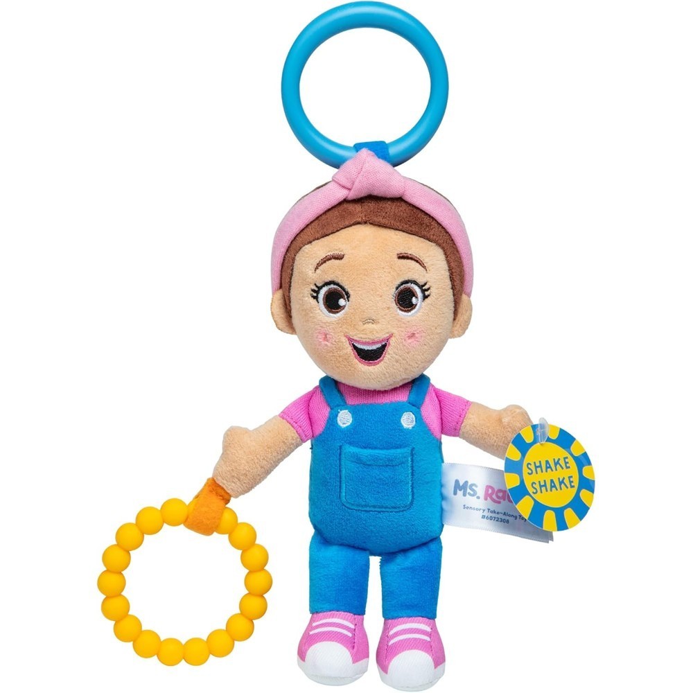 Ms Rachel Official Sensory Take-Along Toy Herbie Doll—features brown hair, blue overalls, a pink headband, and holds a yellow teething ring plus a blue tag that reads “Shake Shake,” with a blue plastic stroller clip attached to its head. Suitable for babies 3 months and up.