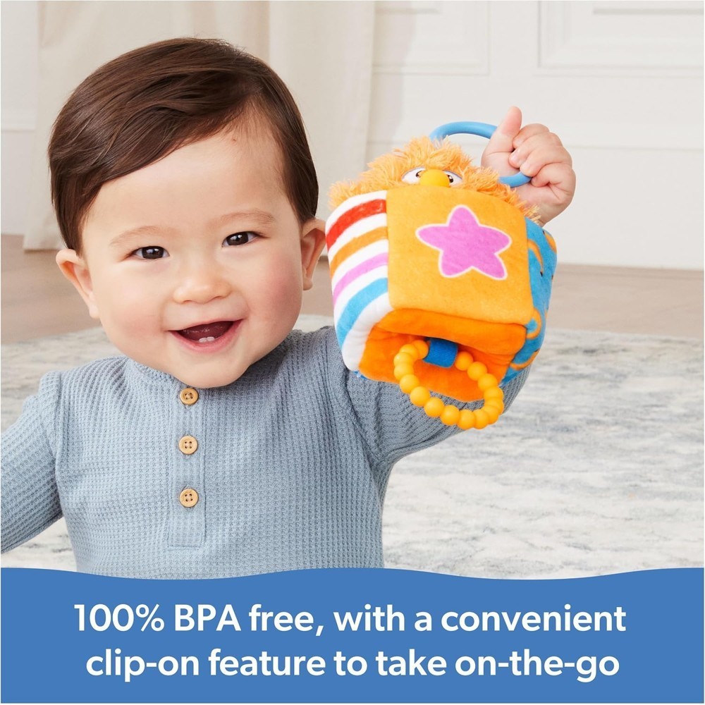 A happy baby sits indoors holding the Ms Rachel Official Sensory Take-Along Toy Herbie Doll—a brightly colored teether rattle with a handle. Text reads: “100% BPA free, with a convenient stroller clip for easy on-the-go use.”.