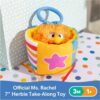A plush orange toy with a blue handle sits in a yellow, star-decorated box on a polka dot surface. Text reads: “Ms Rachel Official Sensory Take-Along Toy Herbie Doll – Baby Teether, Rattle, Stroller Clip, 3 Months+.”.