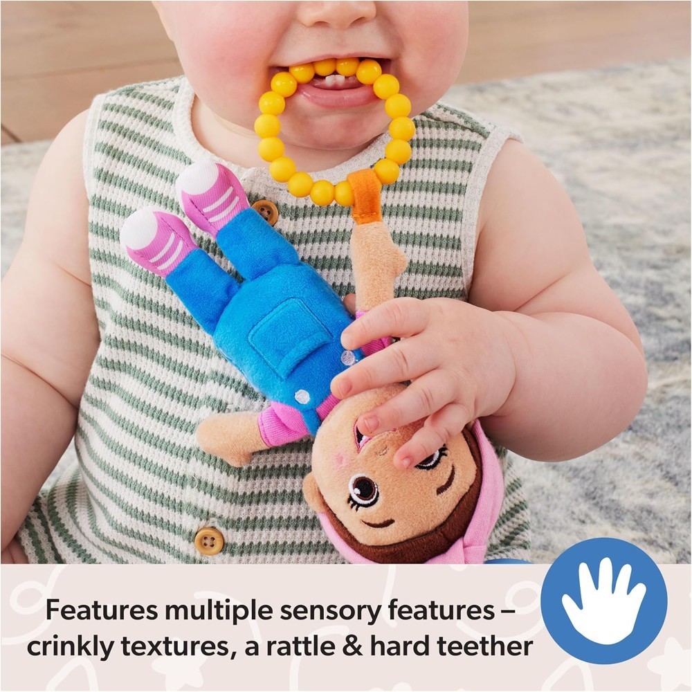 A baby chews on the yellow teether attached to the Ms Rachel Official Sensory Take-Along Toy Herbie Doll while holding it with both hands. Text at the bottom highlights the toy’s sensory features, including its rattle and convenient stroller clip for babies 3 months and up.