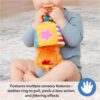 A baby sits on the floor, holding and chewing on the Ms Rachel Official Sensory Take-Along Toy Herbie Doll—a colorful plush teether rattle with a stroller clip, designed for babies 3 months and up.