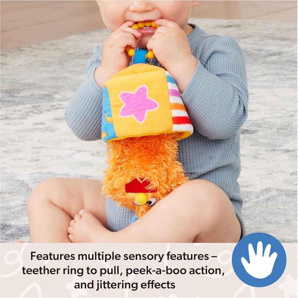 A baby sits on the floor, holding and chewing on the Ms Rachel Official Sensory Take-Along Toy Herbie Doll—a colorful plush teether rattle with a stroller clip, designed for babies 3 months and up.