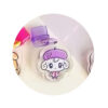 tamagotchi-uni-dustplug-2 Tamagotchi Uni Keychain Dust Plug Acrylic Keychain Charm featuring a cartoon character with white fur, a purple beret, and a pink scarf on a white background, shown next to a purple chair and other partially visible objects.