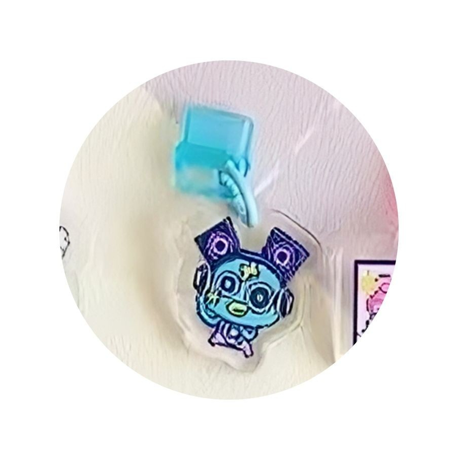 tamagotchi-uni-dustplug-4 A Tamagotchi Uni Keychain Dust Plug acrylic charm is hanging from a light blue hook on a white wall.