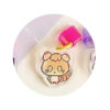 tamagotchi-uni-dustplug-5 A round Tamagotchi Uni Keychain Dust Plug Acrylic Keychain Charm, featuring a cartoon animal with a striped tail, is placed on a light surface next to a pink and a purple plastic item.