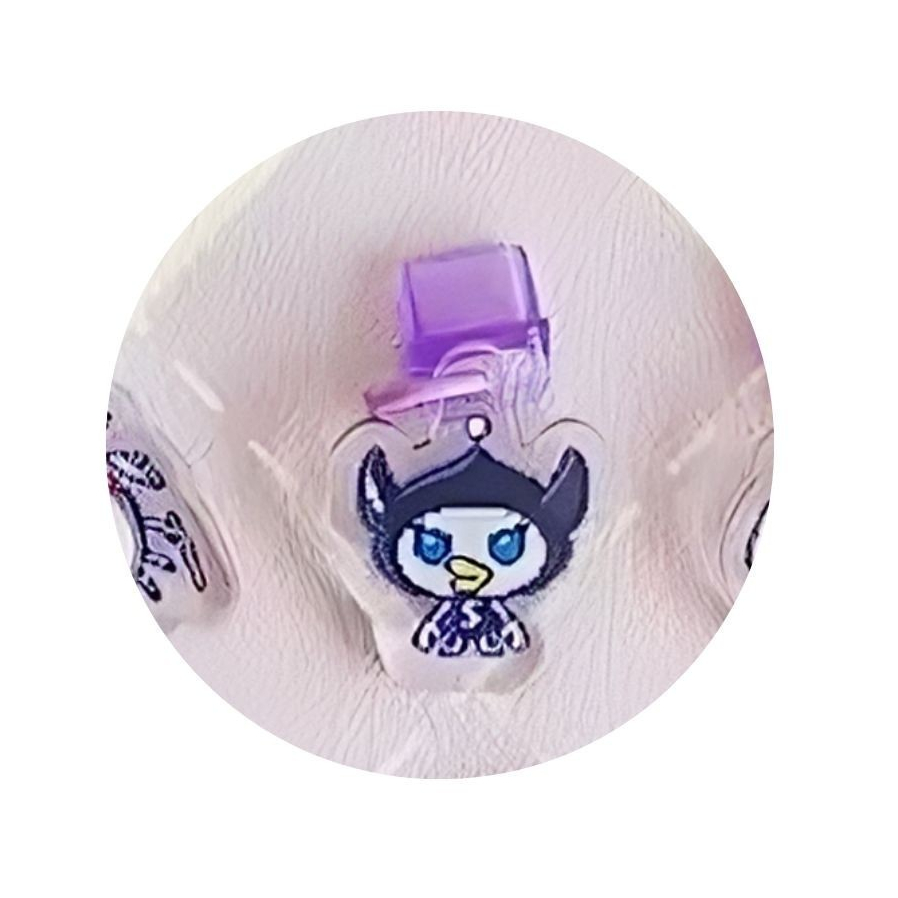 tamagotchi-uni-dustplug-6 A Tamagotchi Uni Keychain Dust Plug acrylic charm featuring a cartoon character with blue eyes, a black hat, and a purple attachment, shown on a textured surface.