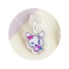 tamagotchi-uni-dustplug-7 Close-up of the Tamagotchi Uni Keychain Dust Plug—an acrylic cartoon bunny charm with purple and pink flowers, attached to a white surface.
